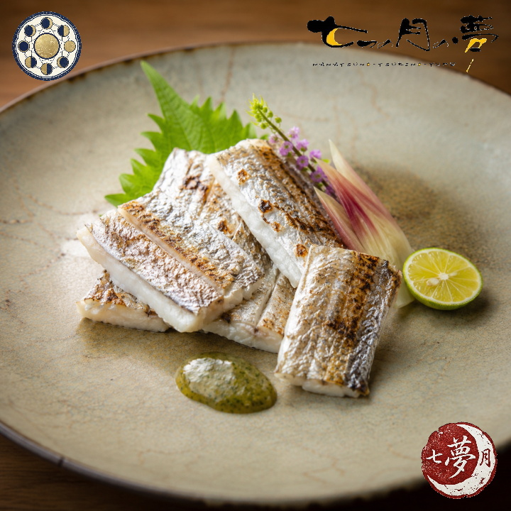 炙り焼きにした太刀魚を美しく盛り付けた和食の一皿。銀色の皮目と白い身が際立ち、季節の薬味や野菜、すだちを添えた上品で落ち着いた創作料理。